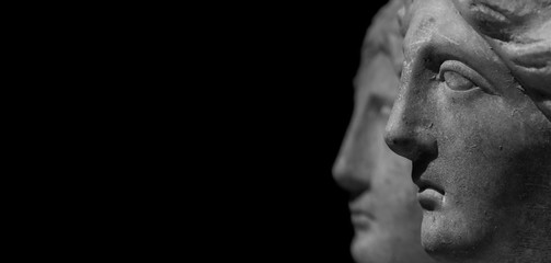 Stone sculpture faces of two statues with a black background